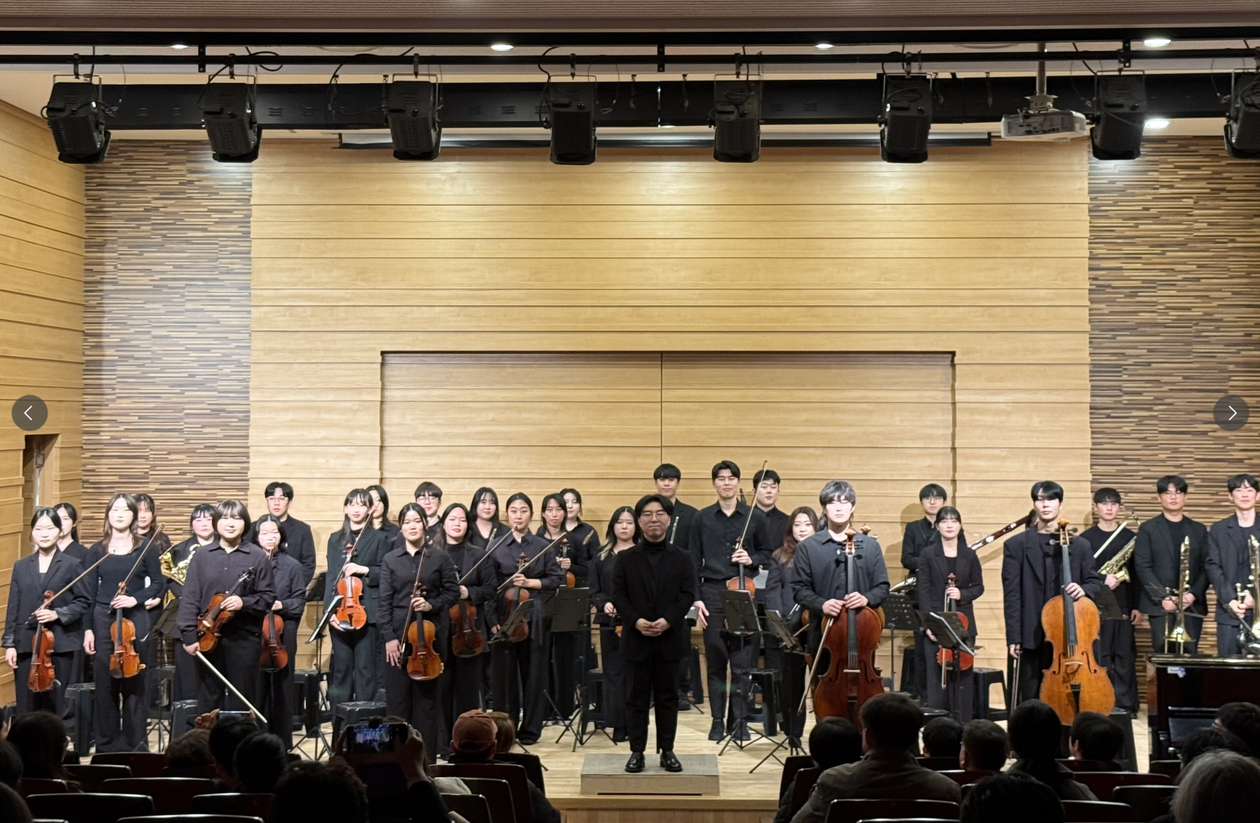 무대 조명 아래 연주하는 대학생 오케스트라의 장면